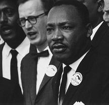 Black man in foreground, Martin Luther King Jr. surrounded by other men 