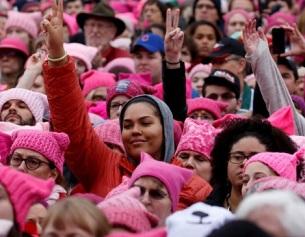 Lots of young women of different races wearing pink in a huge crowd with peace signs with their fingers in the air