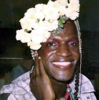 Photo of black woman smiling with her hand by her cheek and lots of white flowers in her hair