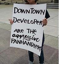 Sign being held outside reading Downtown developers are the aggressive panhandlers