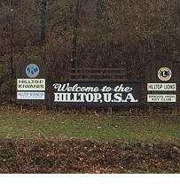 Long outdoor sign in front of trees saying Welcome to the Hilltop USA