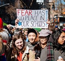 Young people wearing winter coats one young man holding a sign above his head that says Fear has no place in our schools