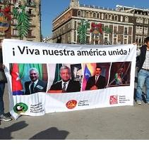 People holding a big banner outside that says Viva nuestra america unida! and a lot of faces of people