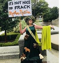 Woman in a long green dress with a sash and a cape and crown of flowers with a sign saying It's not nice to frack mother nature