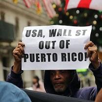 Black man holding a sign above his head saying USA, Wall St. Out of Puerto Rico