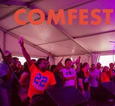 Purplish and reddish hues in a photo of several young people, black and white, holding their fingers as peace signs in the air, cheering and clapping under a tent with the words COMFEST in orange at top