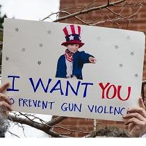 Someone holding up a sign with a picture of a young boy dressed like Uncle Sam and the words I WANT YOU to prevent gun violence