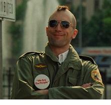 Robert De Niro, youngish white man with a mohawk hairsut and sunglasses smiling with his arms crossed, wearing an army jacket with patches