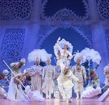 Fancy costumed people against blue theater backdrop like a castle inside, feathered headdresses, dancing