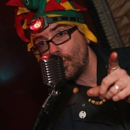 Man with glasses in a colorful hat talking into a mic