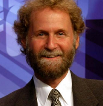 Photo of man with light brown curly hair and moustache and beard smiling in a suit