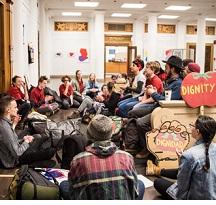 Dozens of kids sitting around an office with a tomato sign that says Dignity