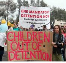 People outside at a rally holding signs saying Children out of detention and End Mandatory Detention Now
