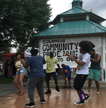 Young black people dancing outside in front of a gazebo with a Columbus Community Pride banner