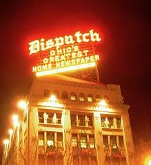 Bright yellow and red neon sign saying Dispatch Ohio's greatest homes newspaper above a big fancy building at night