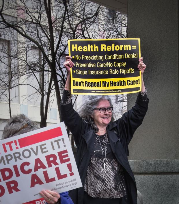 Gray haired woman holding protest sign above head asking for Health Reform