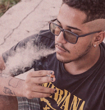 Young black man with glasses blowing smoke out of his mouth with a cigarette in his hand