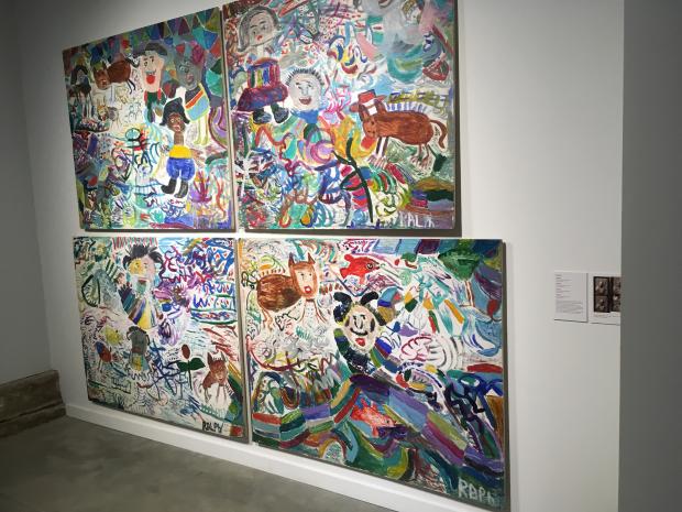 Paintings hanging on a white wall that are very large one on top of the other and of very colorful scenes