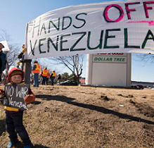 Big banner outside saying Hands off Venezuela and very small boy holding sign saying No War Venezuela