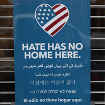 Blue sign with a heart that has a flag and words Hate has no home here