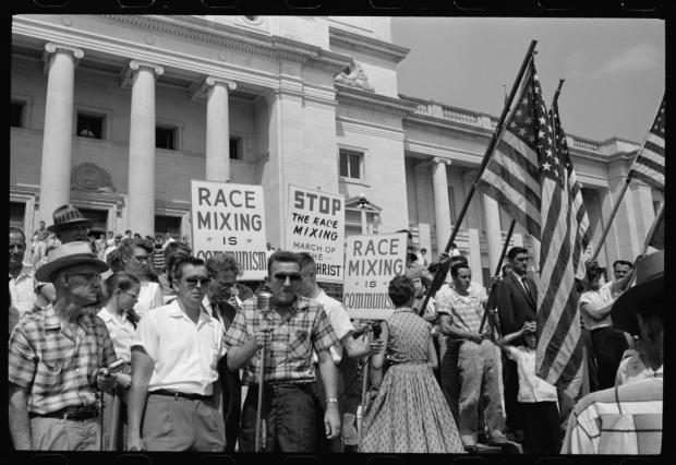 Black and white photo of protest in streets from 50s with sign saying something about race mixing