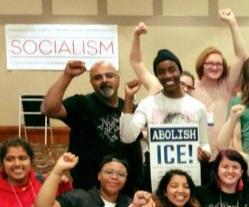 People smiling with fists in the air and a sign that says Socialism and one that says Abolish ICE