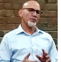Bald white man with glasses with white goatee talking and making hand gestures