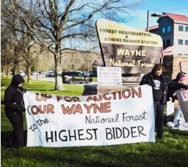 People holding banner outside of Wayne National Forest saying Up for Auction Our Wayne National Forest to the Highest Bidder