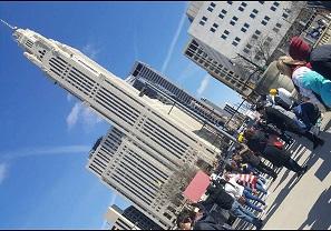 Sideways photo of downtown skyscraper with people standing below protesting
