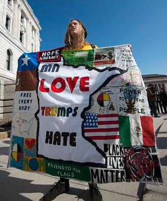 A woman protests Donald Trump with a "Love Trumps Hate" banner/blanket