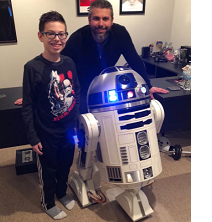 Man and young boy posing next to a robot that has a round top and white round body