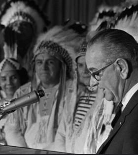 Lyndon Johnson at a mic and Native men in background