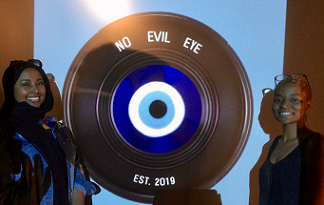 Black woman standing next to a large film reel that says No Evil Eye on it