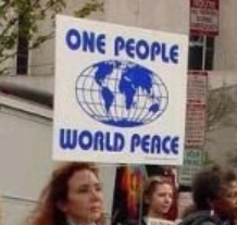 Woman outside with others holding a sign on a stick that has a globe in the middle and the words One People World Peace
