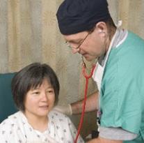 Doctor with scrubs on using stethoscope on a middle aged Asian woman