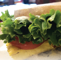 Close up of a sandwich with lettuce and tomato spilling out the side