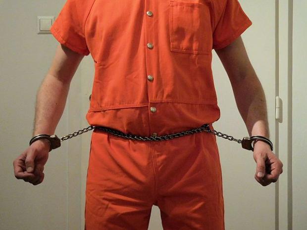 Guy in orange jumpsuit and chain around his belly attached to his wrists