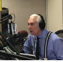 Gray haired white man in blue shirt wearing headphones talking into an elaborate microphone set up