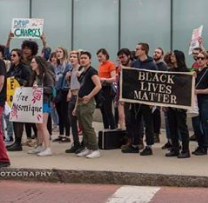 Several young people on a sidewalk at a rally holding a banner saying Black Lives Matter