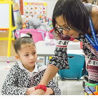 Teacher leaning over showing something to small child