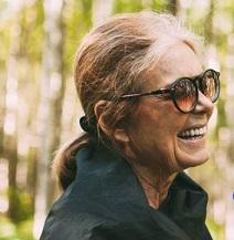 Older woman with big sunglasses facing right in a ponytail, smiling