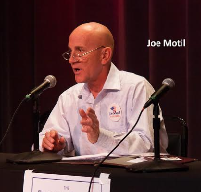 White man with glasses and a white shirt talking into a mic at a table making a hand gesture with the words Joe Motil