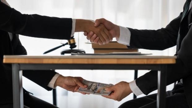 Two men shaking hands above the table and exchanging money under the table