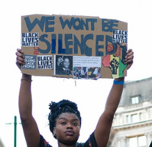 Black woman holding up a sign that says we will not be silenced