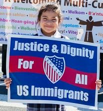 Very young Latino-looking girl holding a red white and blue sign that says Justice & Dignity for all US immigrants