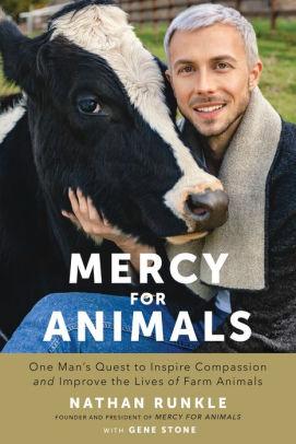 A man with white hair and goatee standing outside petting a black cow who has a white stripe up her nose and the word Mercy below