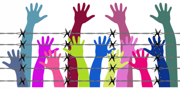 Different color arms and hands reaching up behind a barbed wire fence