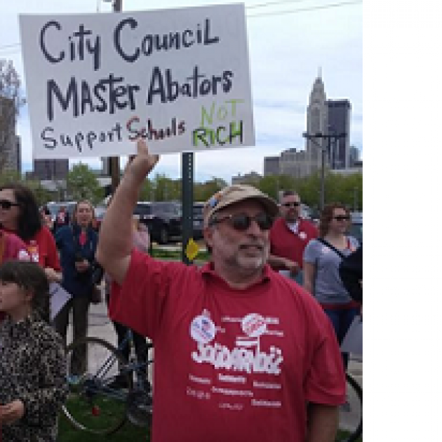 White man with sunglasses, a gray beard and a baseball cap wearing a Solidarity T-shirt is outside among lots of people with downtown Columbus in the background, holding a sign that says City Council Master Abators Support Schools not the Rich