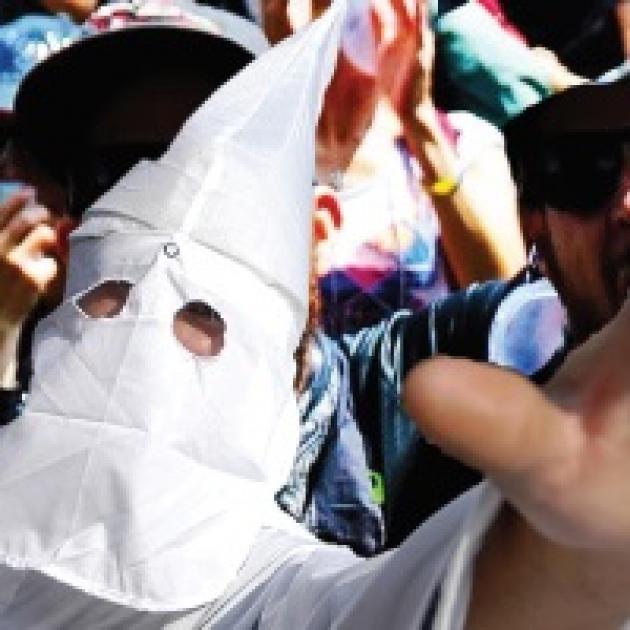 Klan member in pointy white mask holding his hand in the air