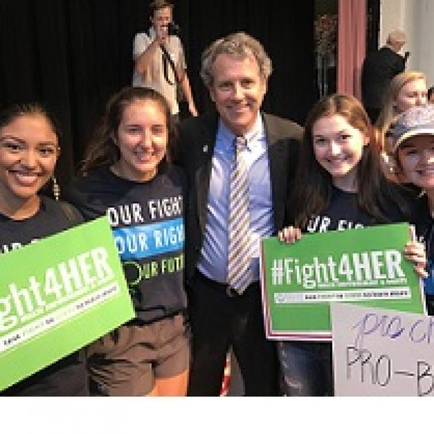Three young women with #Fight4HER signs and one older white man in a suit